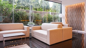Uma sala de estar moderna com sofá, mesa de centro e vista para um jardim através de grandes janelas.