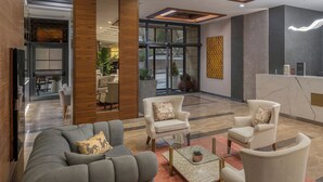 A modern lobby with a grey sofa, armchairs, a reception desk, and a glass coffee table. - Mercure Ankara Kızılay (Ankara)
