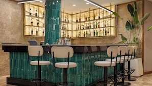 A bar area with a green bar counter, multiple shelves of liquor bottles, and four bar stools. - Mercure Ankara Kızılay (Ankara)