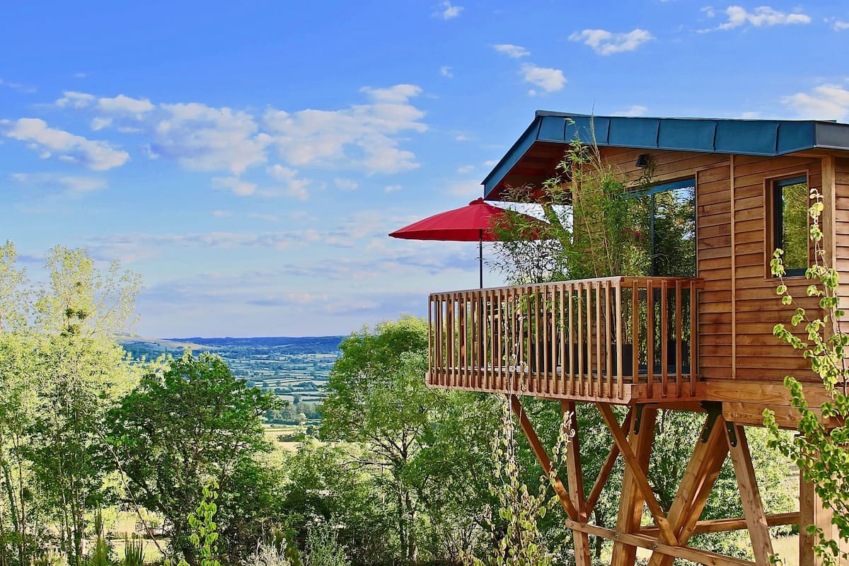 Une cabane en bois dotée d’un balcon, entourée de verdure et offrant une vue sur le paysage.