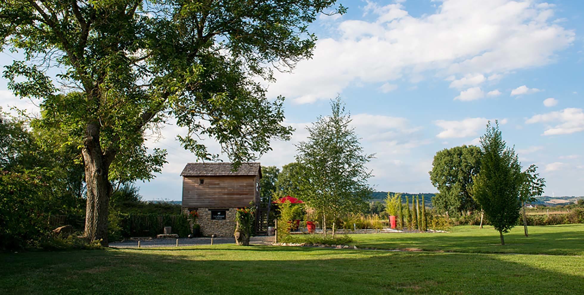 A rustic wooden building with a stone foundation, surrounded by a well-maintained lawn and trees.