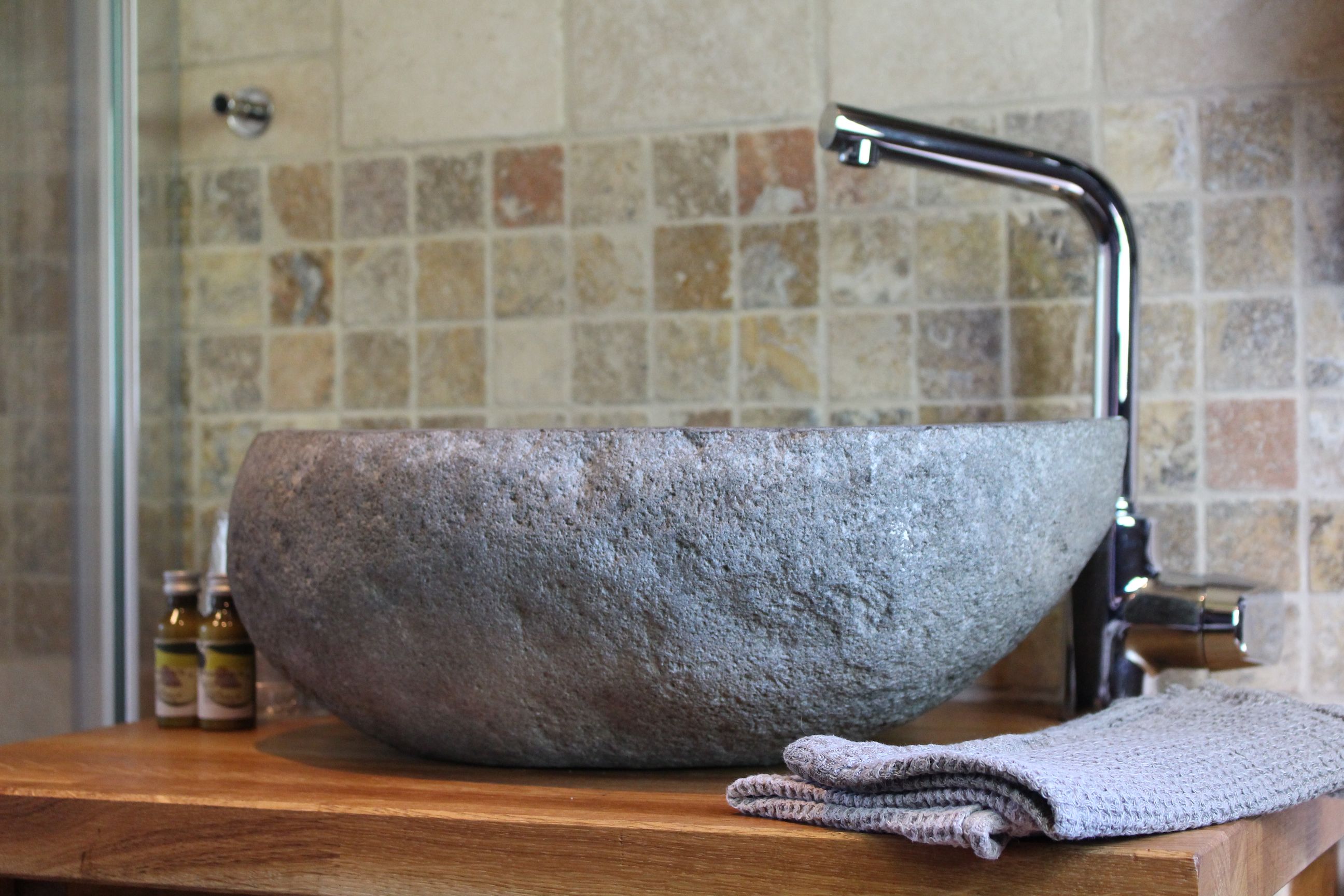 A stone sink with a modern faucet in a bathroom with tiled walls.
