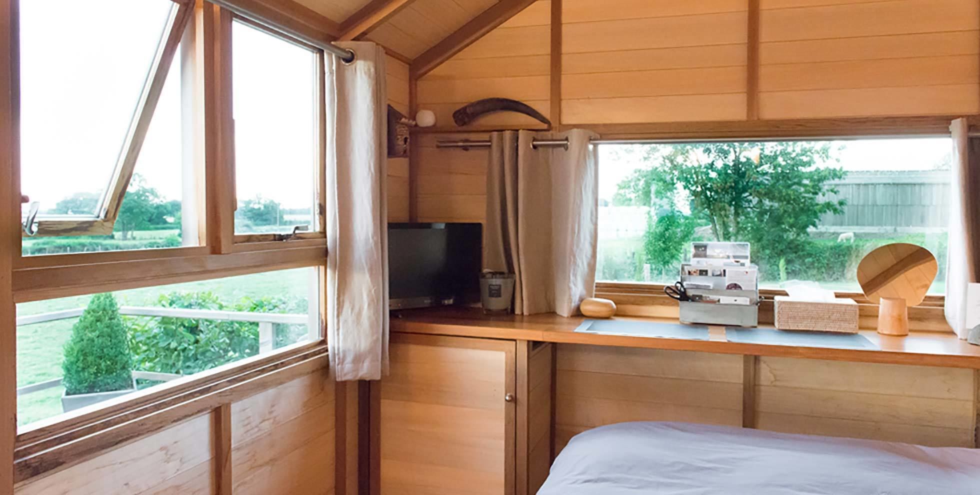 Una habitación con una cama, un escritorio con computadora, un televisor y un ventanal con cortinas.