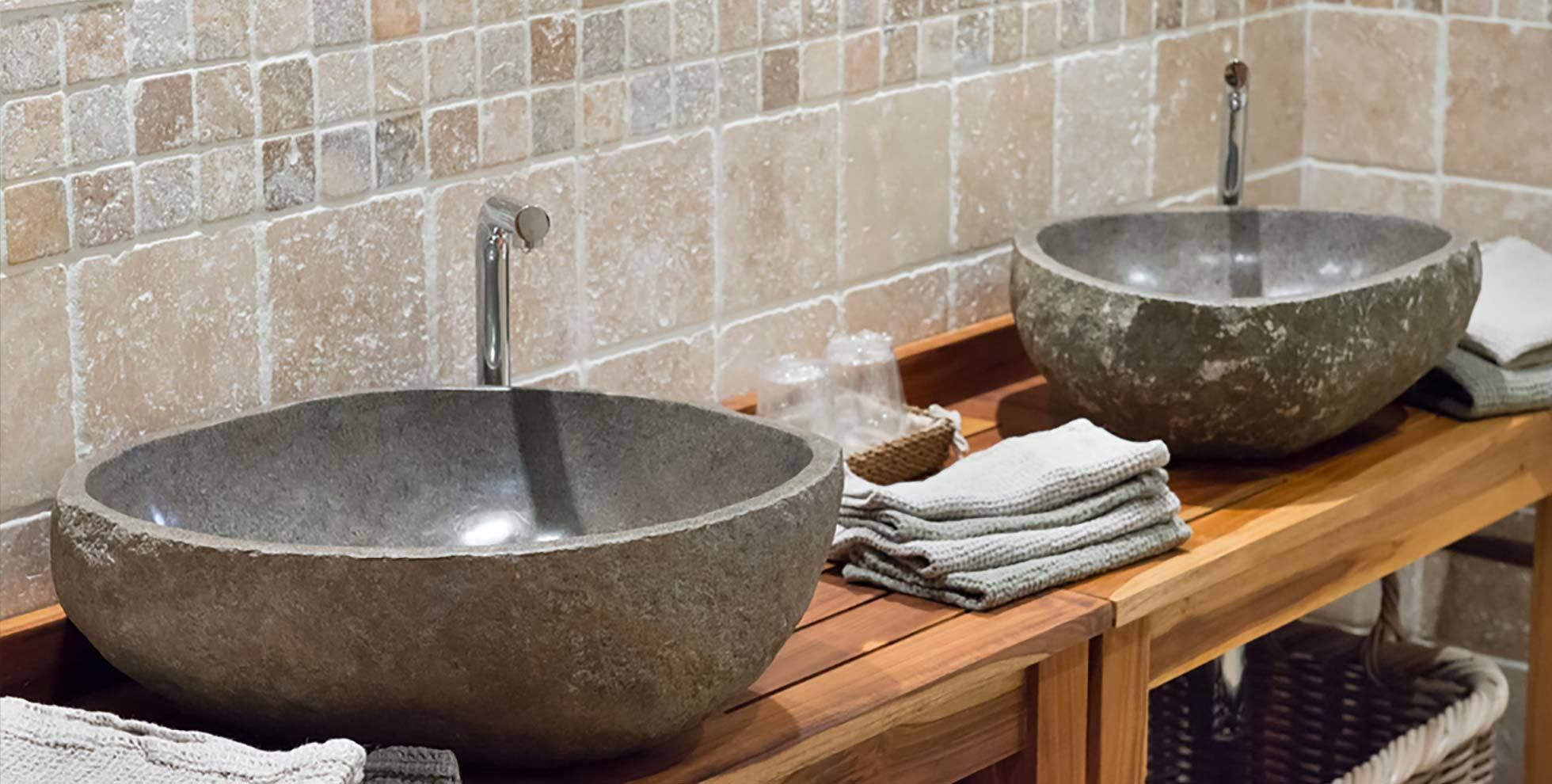 Two large, round stone sinks with faucets, placed on a wooden counter with towels and a basket.
