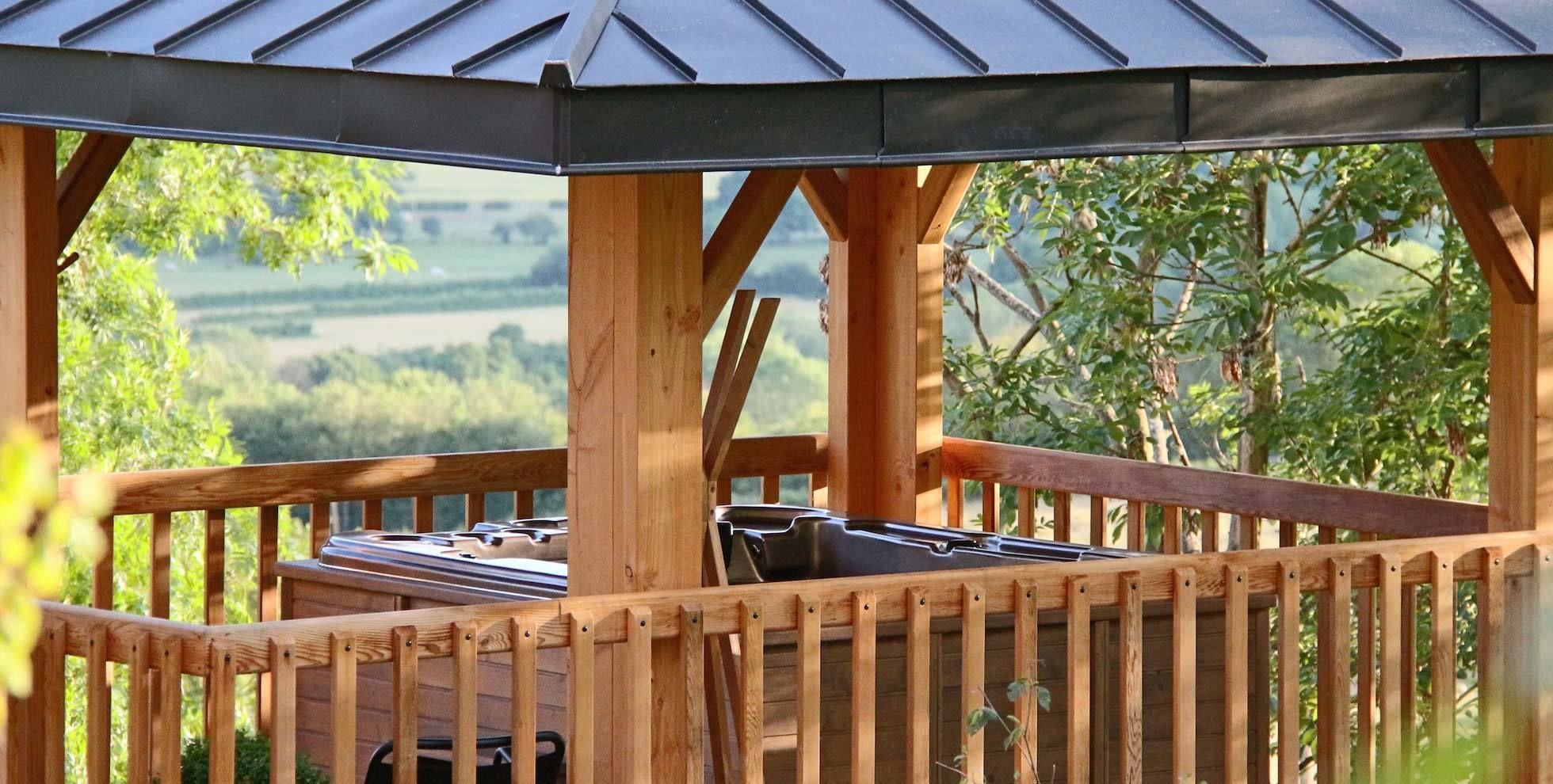 Una terraza de madera con techo metálico, que da a un paisaje verde.