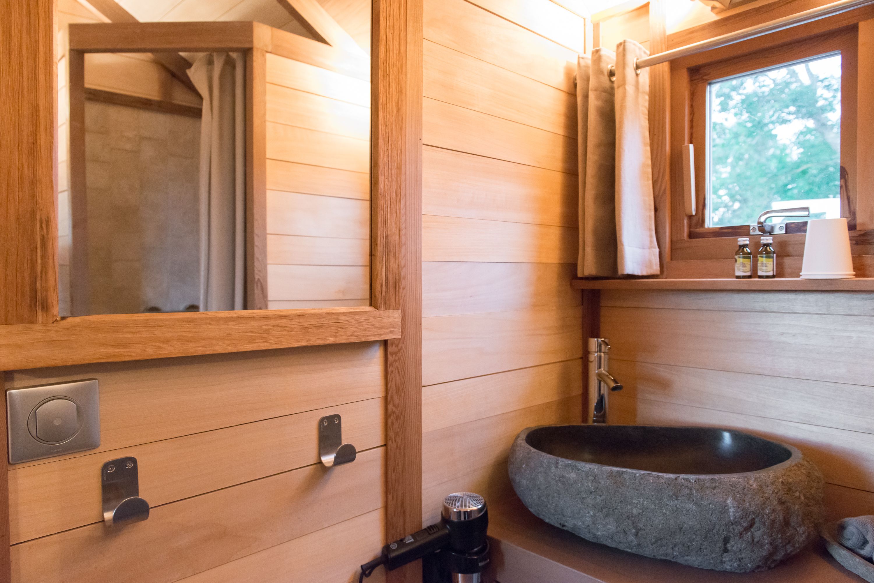 Ein Badezimmer einer Holzhütte mit einem Steinsink, Holzschränken und einem Fenster mit Blick auf Bäume.