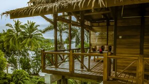 A wooden deck with a thatched roof overlooking a lush garden and a body of water. - Janji Laut Resort (Tombariri)