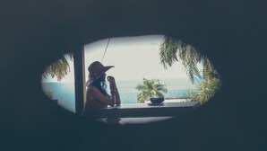 A person sitting by a window overlooking a body of water, with a palm tree visible outside. - Janji Laut Resort (Tombariri)