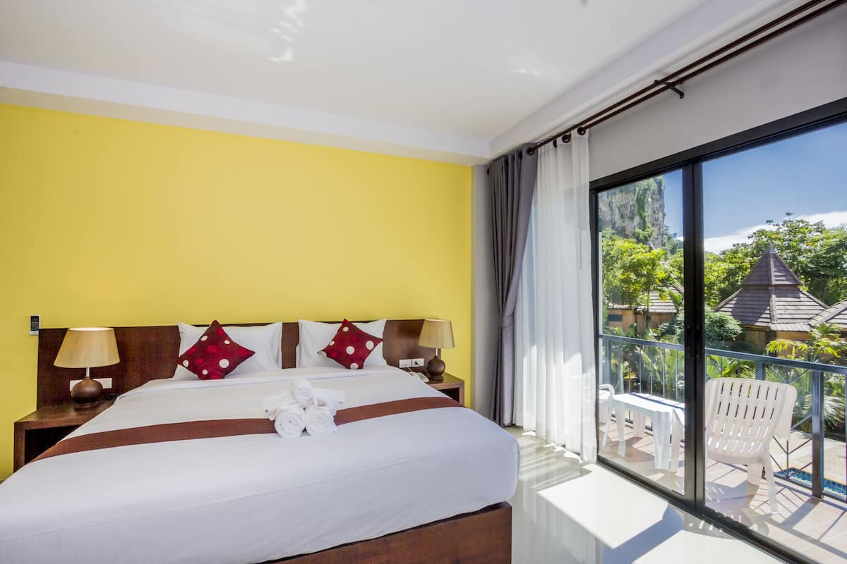 A hotel room with a large bed, two bedside tables with lamps, a view of the outdoors through a balcony, and a window with curtains.