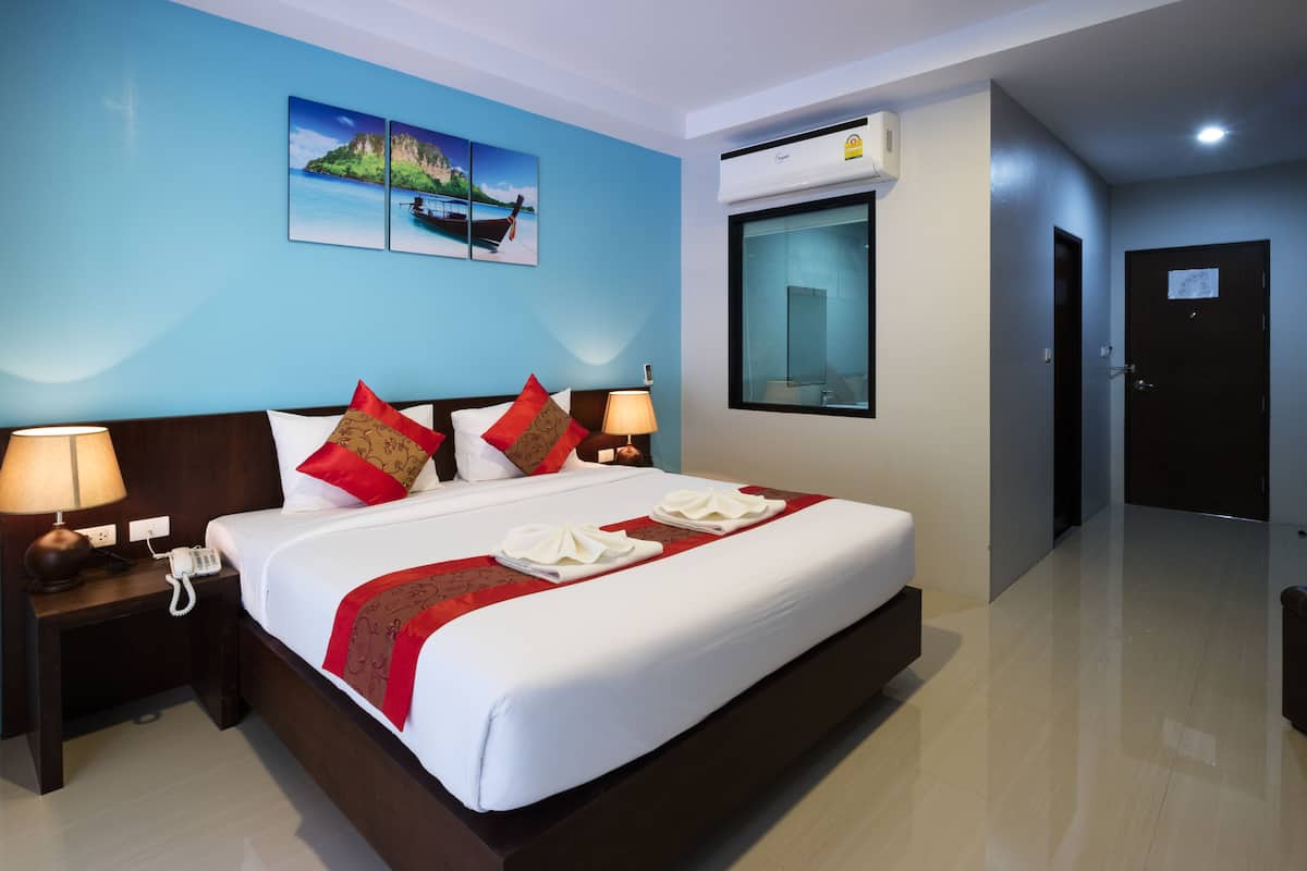 A hotel room with a large bed, a nightstand with a phone, a window with an air conditioner, and a door.