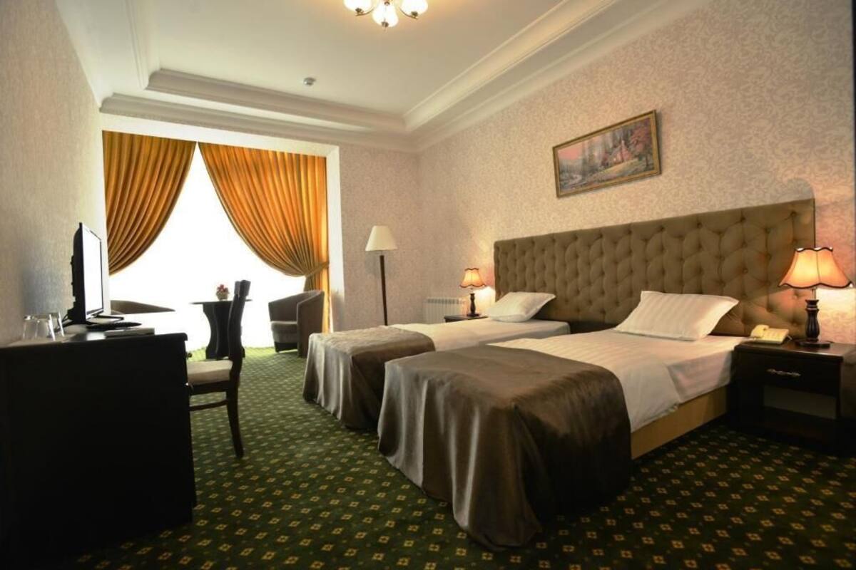 A hotel room with two beds, a desk, a chair, a lamp, and a painting on the wall.