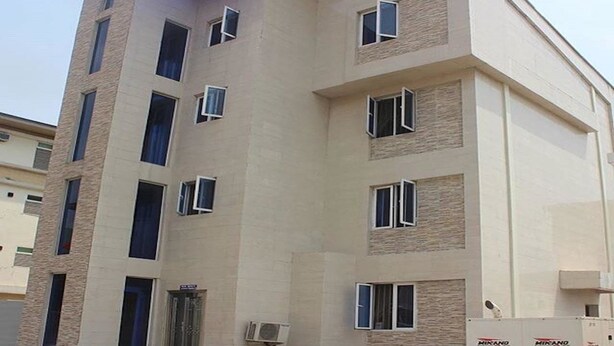 A multi-story building with a beige facade, multiple windows, and a visible entrance with a door. - Magmercy Apartments (Lagos)
