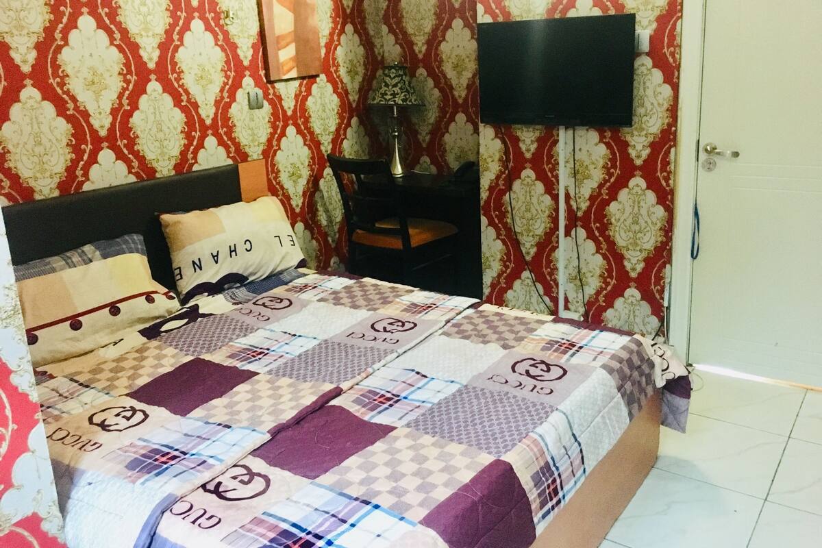 A bedroom with a bed, pillows, a TV, and a patterned wall.