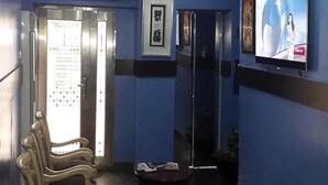 A lobby with a reception desk, a bench, a television screen, and an elevator. - Magmercy Apartments (Lagos)