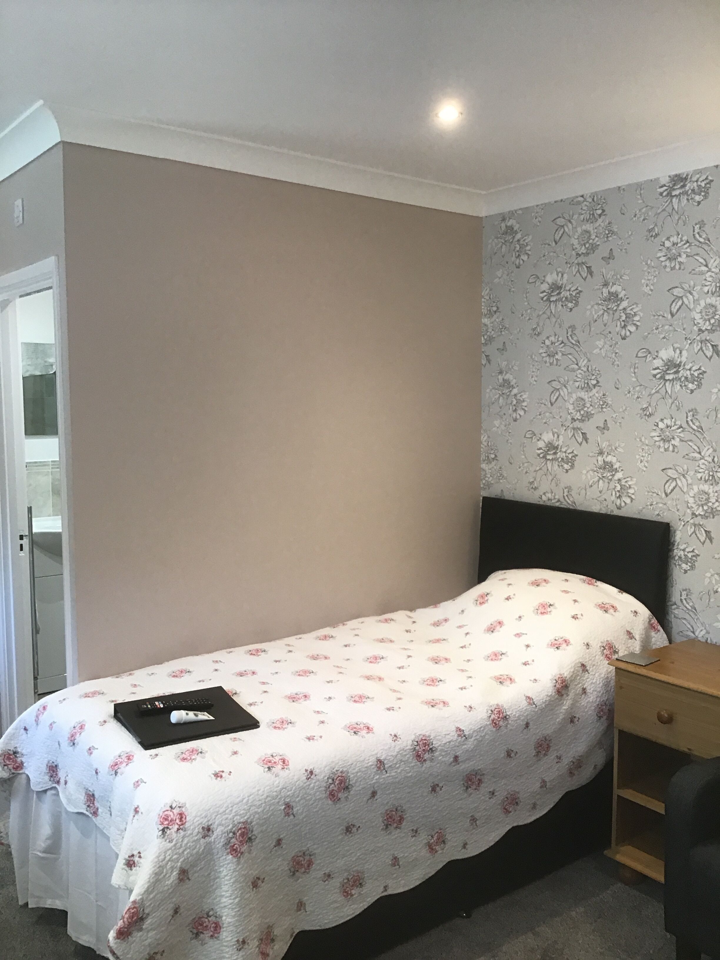 A bedroom with a single bed, a wooden nightstand, and a door leading to a bathroom.