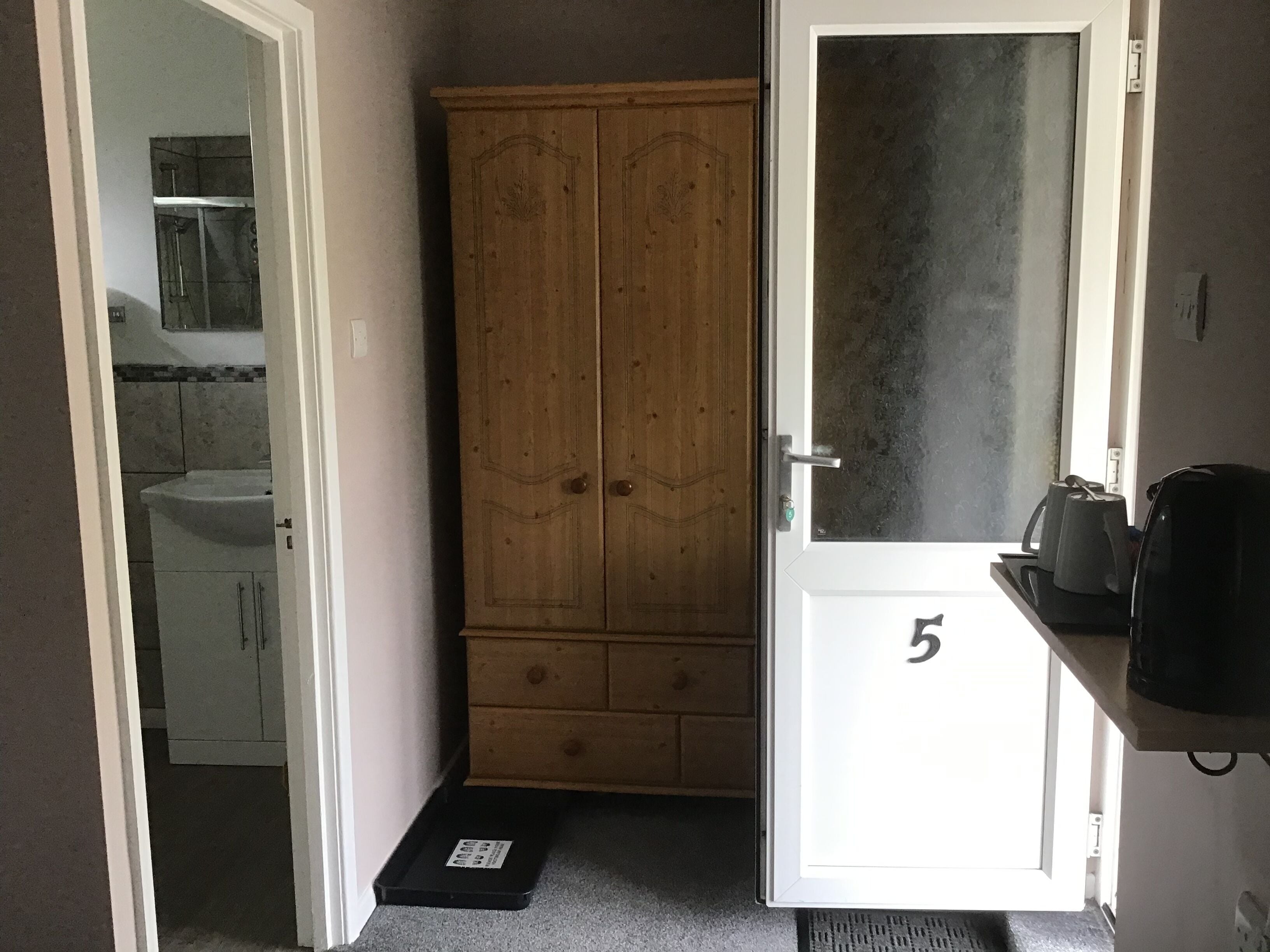 Un pasillo estrecho con un armario de madera, una puerta blanca con el número 5, y una cocina visible a través de una puerta abierta.