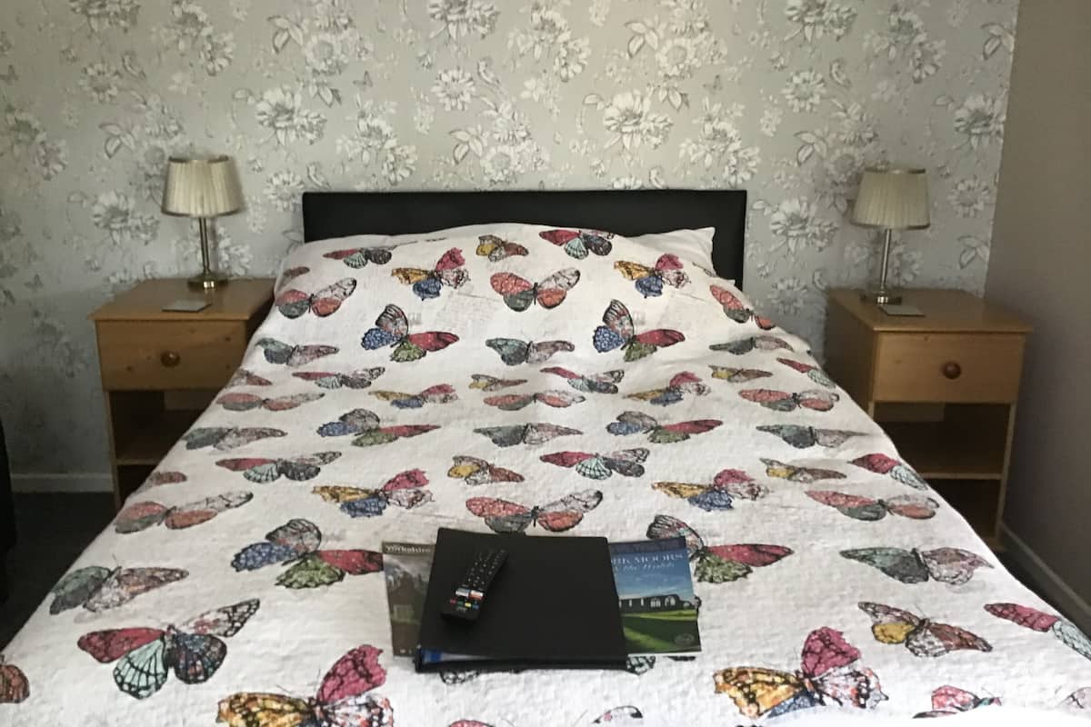 A bed with a butterfly-patterned duvet, two bedside tables with lamps, and a book on the bed.
