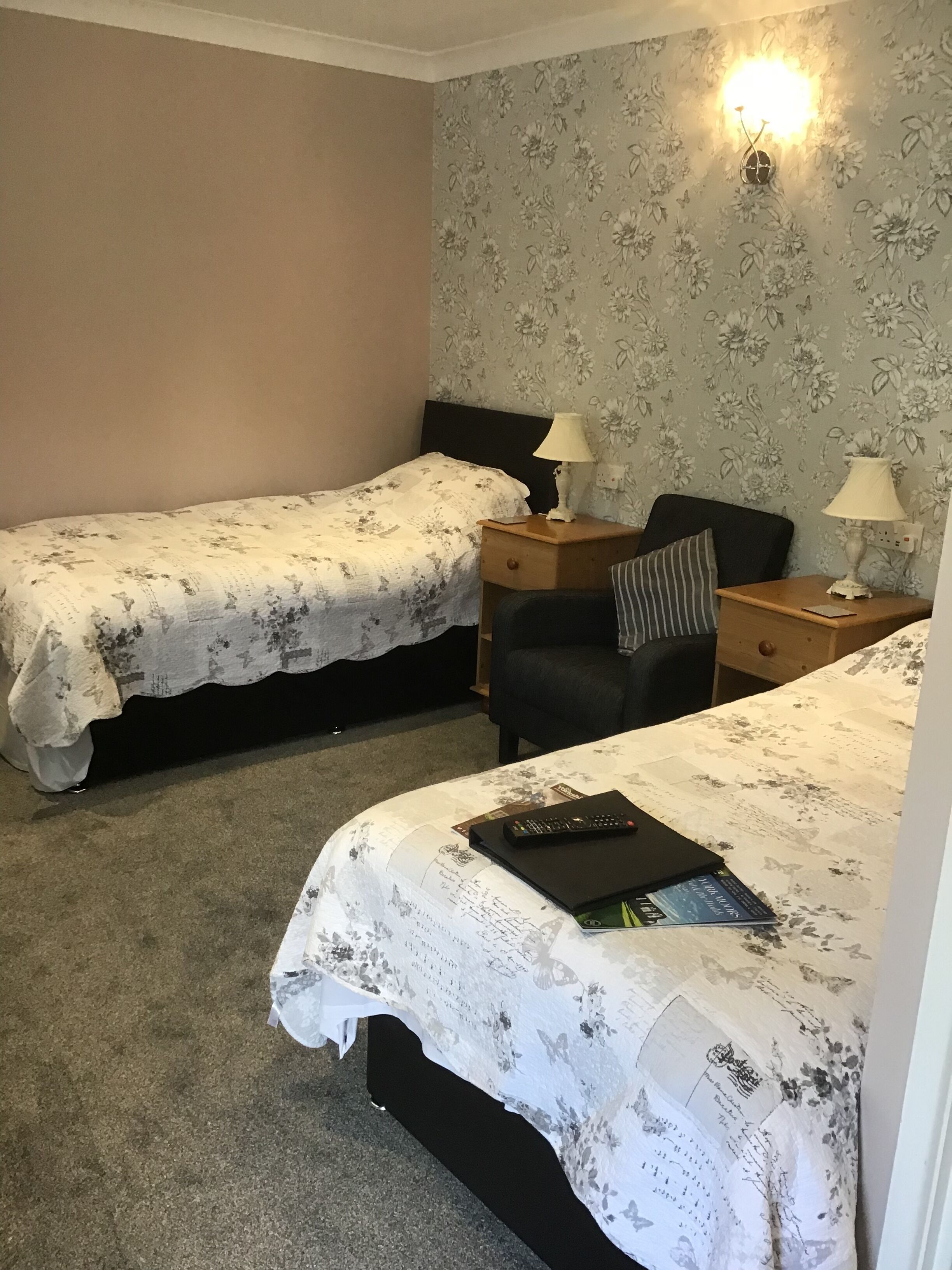 A bedroom with two single beds, a nightstand with lamps, a chair, and a small table.