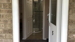 A hallway leading to a bathroom with a glass shower enclosure, a white door, and a number 5 on the door. - The New Inn Motel (York)