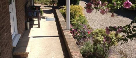 A covered porch with a bench, a brick wall, and a garden with various plants and flowers.