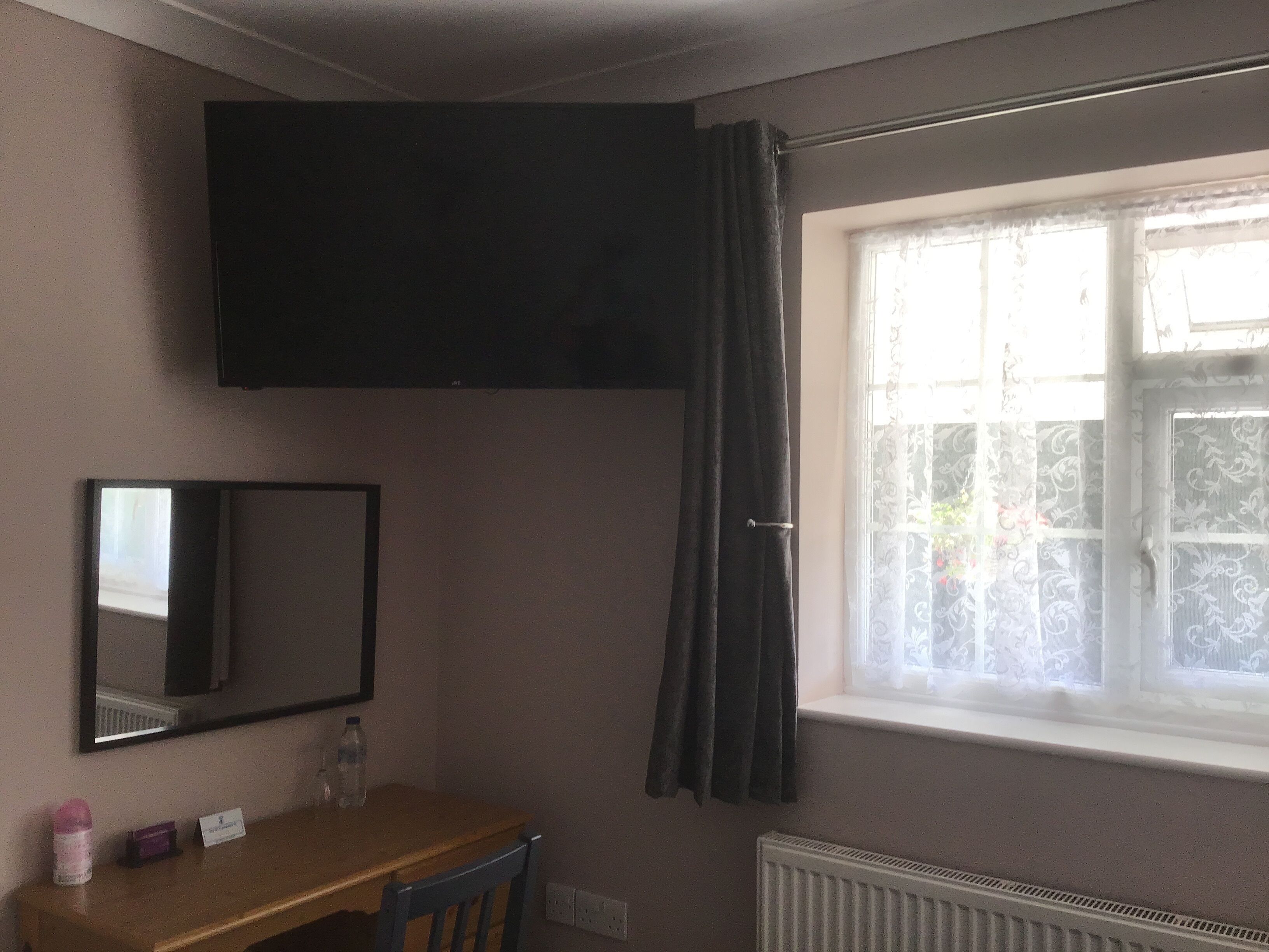 Una habitación con una mesa de madera, un espejo, un televisor de pantalla plana montado en la pared y una ventana con cortina.