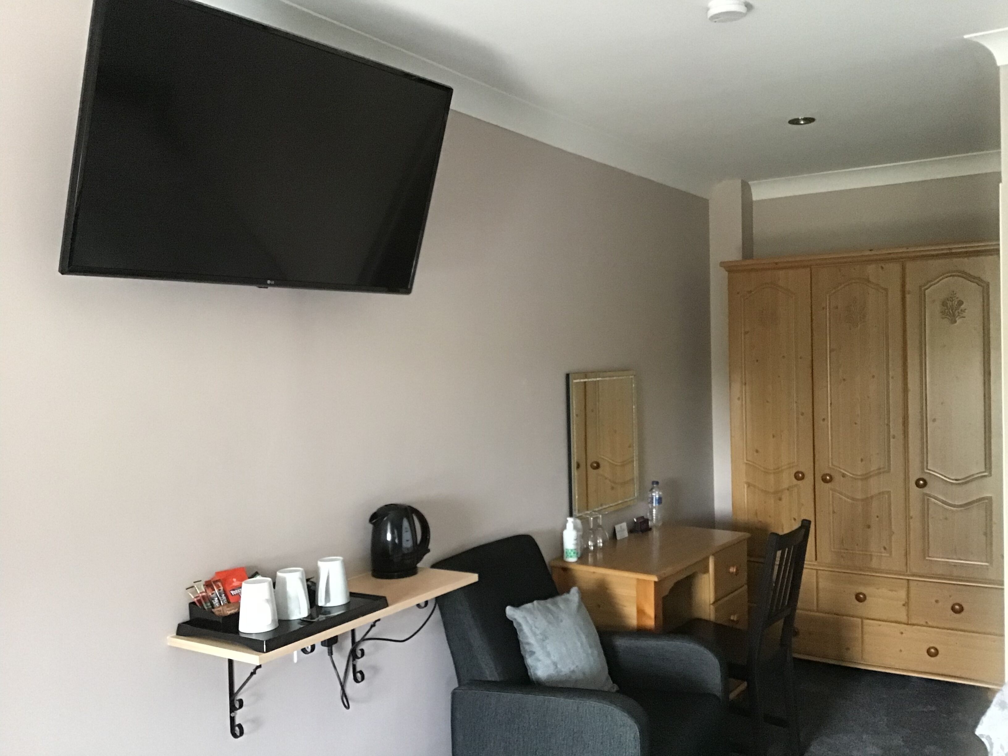 Habitació amb televisió de pantalla plana penjada a la paret, escriptori de fusta amb una cadira, sofà i armari.