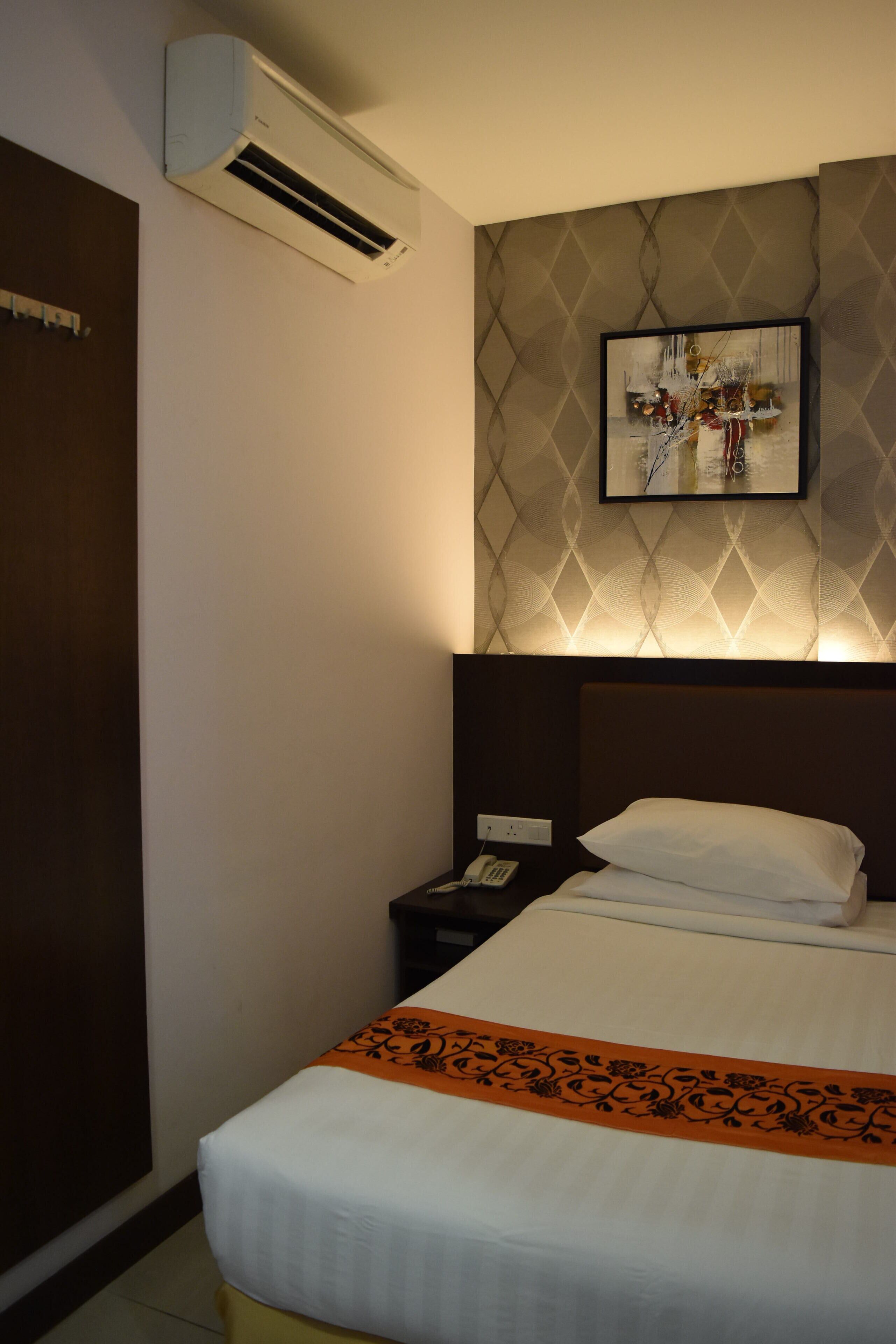 A hotel room with a bed, a nightstand, an air conditioning unit, and a framed artwork on the wall.