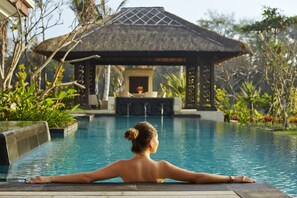 A woman relaxing by a pool with a thatched-roof structure in the background. - Bali National Golf Villas (Nusa Dua)