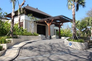 A modern building with a covered entrance, stone walls, and palm trees. - Bali National Golf Villas (Nusa Dua)