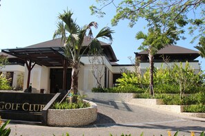 A modern building with a covered entrance, a stone wall, and a sign that reads "GOLF CLUB". - Bali National Golf Villas (Nusa Dua)