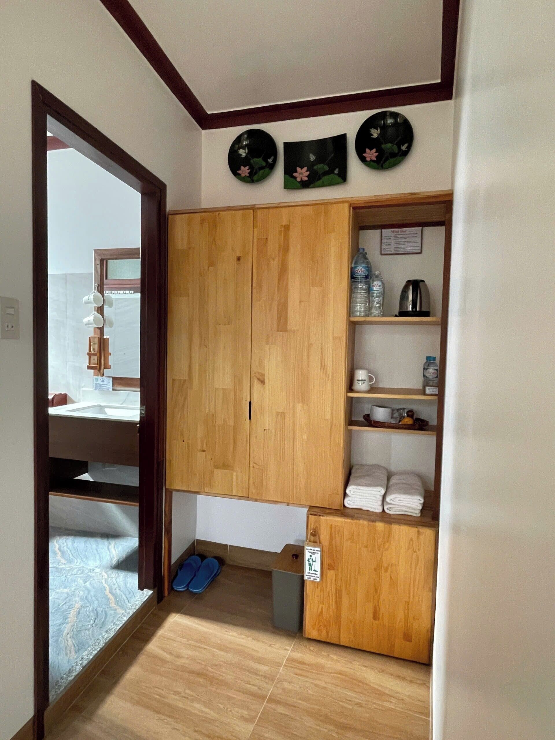 A room with a wooden wardrobe, a shelf with toiletries, and a pair of slippers.