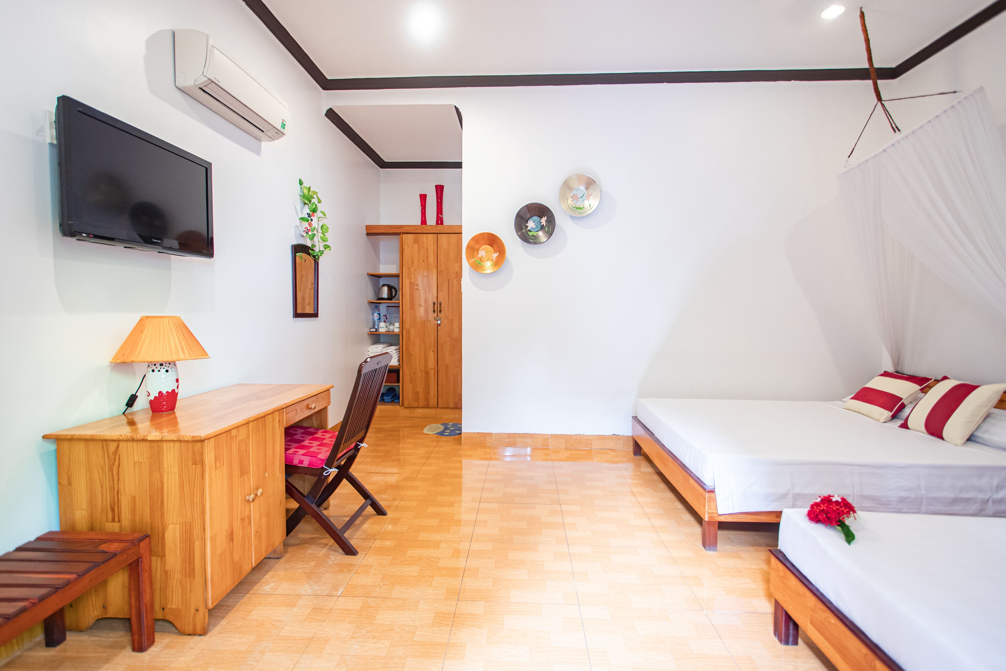 Un dormitorio con cama, mesita de noche, lámpara, escritorio de madera, silla y televisor.