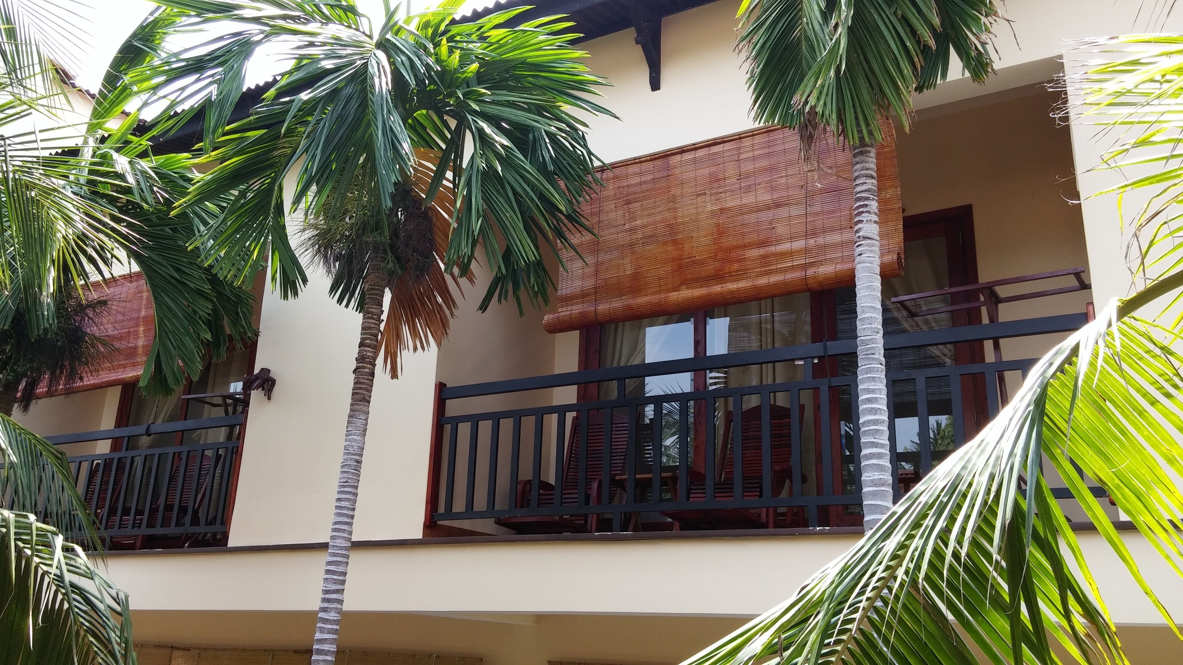 A building with balconies, palm trees, and a bamboo awning.