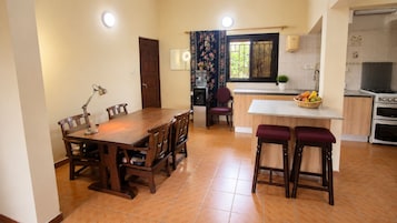 A dining area with a wooden table and chairs, a kitchen with a stove and oven, and a window with curtains.