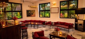 Una habitación con un sofá rojo curvo, varias mesas, una zona de bar y ventanas amplias con vistas a zonas verdes.