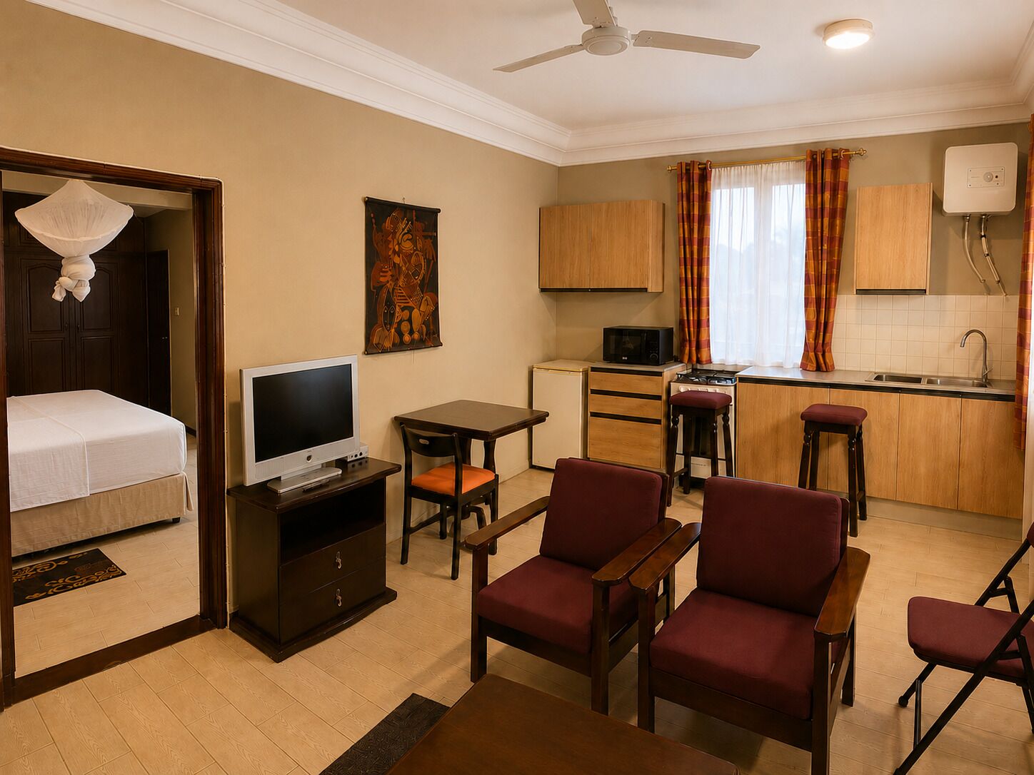 Ein kleines Hotelzimmer mit Bett, Fernseher, Sitzgelegenheit, Kochnische und Deckenventilator.