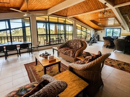 Amplia sala de estar con techo alto, ventanas grandes y comedor con vistas al exterior.