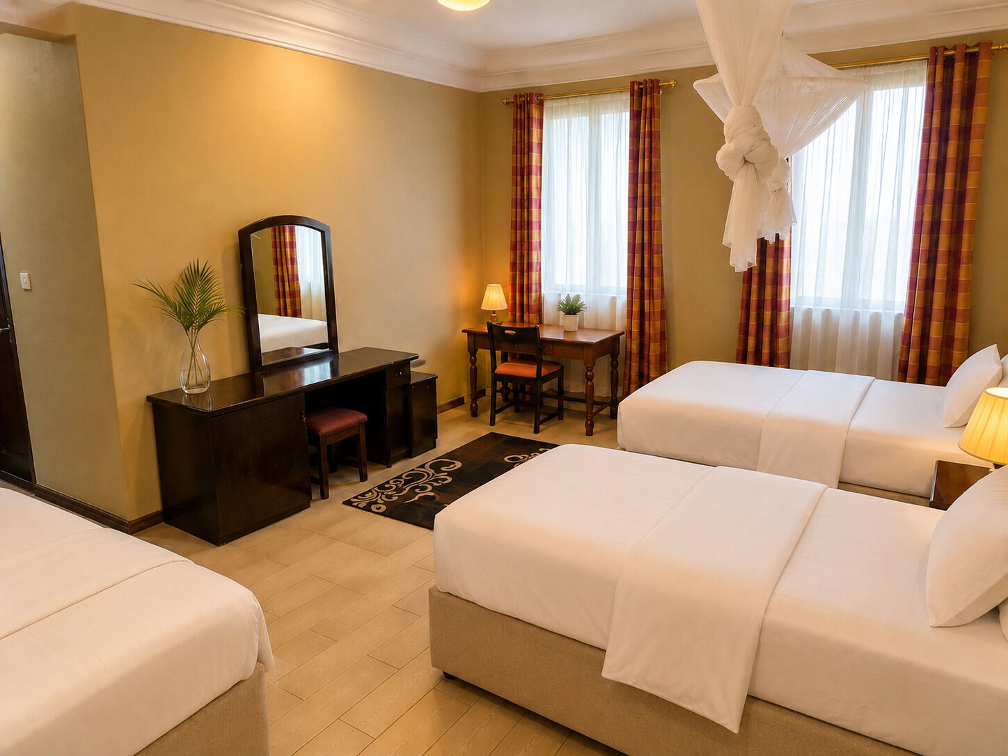 A hotel room with two beds, a desk, a chair, a mirror, and a window with curtains.