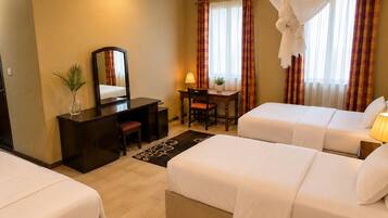 A hotel room with two beds, a desk, a chair, a mirror, and a window with curtains.