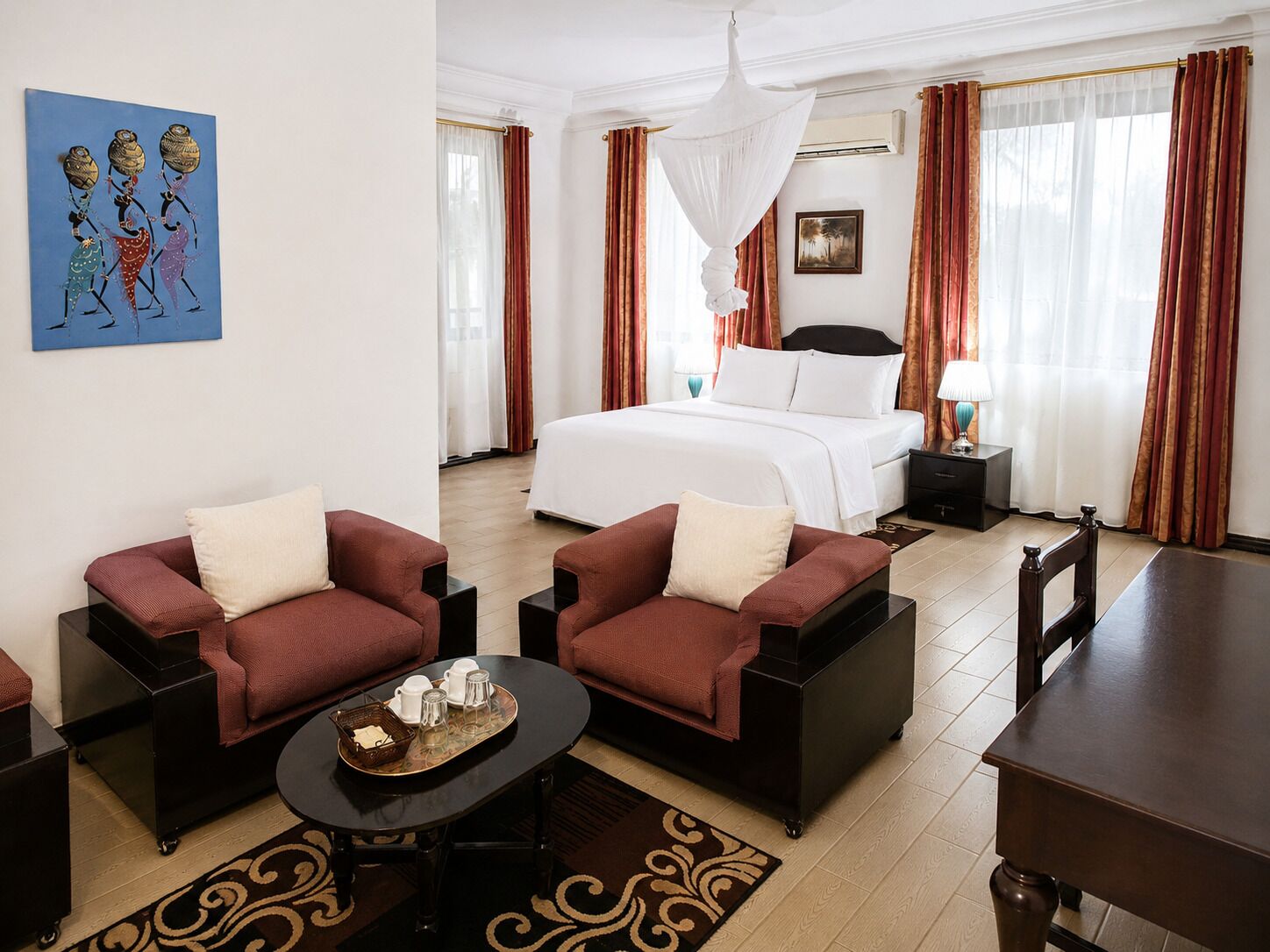 A hotel room with a bed, two sofas, a coffee table, a nightstand, and a painting on the wall.