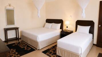 A hotel room with two single beds, a bedside table with a lamp, a mirror, and a decorative rug.
