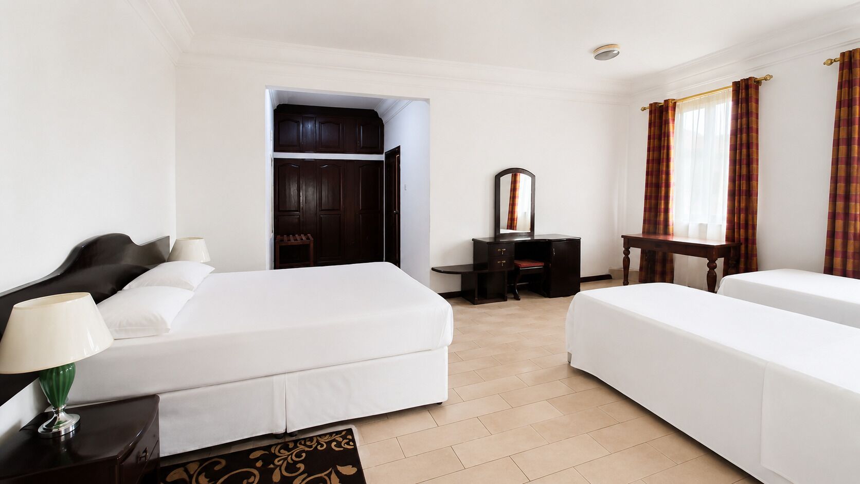 A hotel room with two beds, a desk, a mirror, and a wardrobe.
