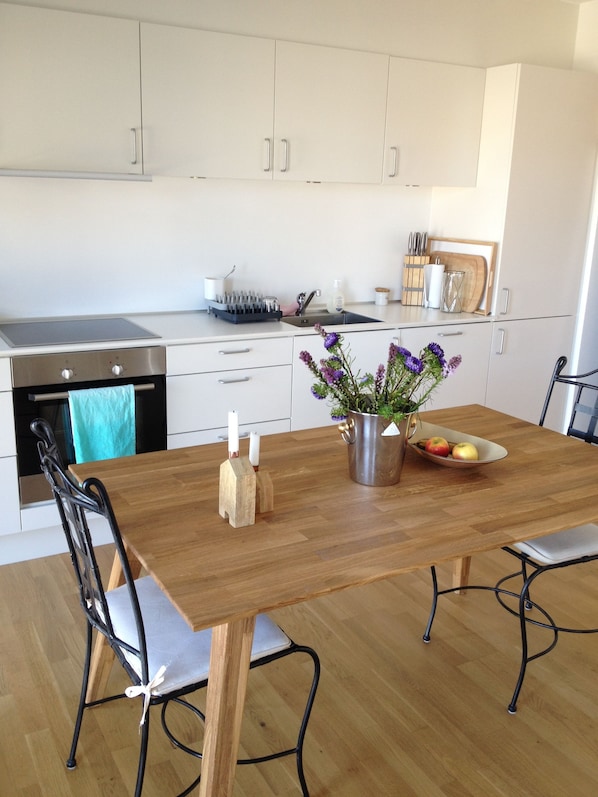 Une cuisine moderne avec des meubles blancs, un four en acier inoxydable, un évier et une table à manger avec des chaises.