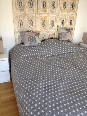 Un lit bien fait, recouvert d’une couvre-lit à motifs étoilés, avec une tête de lit ornée de motifs végétaux et plusieurs oreillers.
