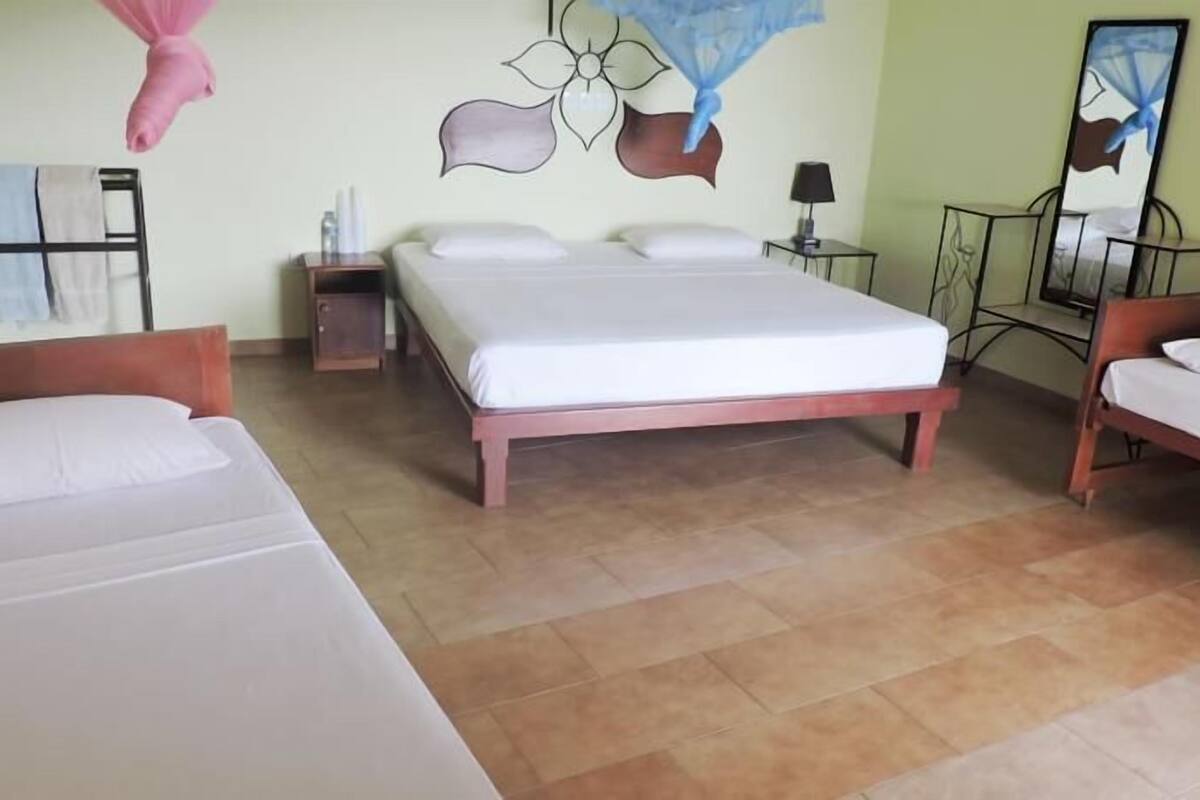 Habitación de hotel con dos camas, cabecero de madera, mesita de noche, lámpara y un cuadro floral en la pared.