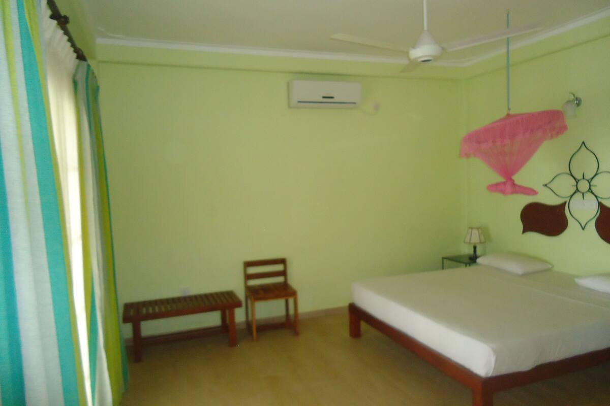 Un dormitorio con cama, un banco, una mesita de noche, una lámpara y un adorno de pared.