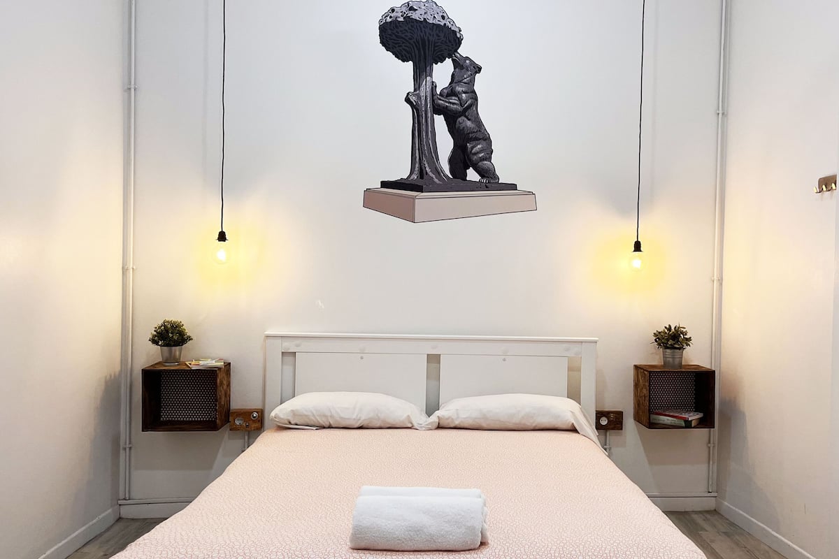 Ein modernes Schlafzimmer mit einem Bett, zwei Nachttischen mit Pflanzen, einem Kopfteil und einer Wandskulptur.