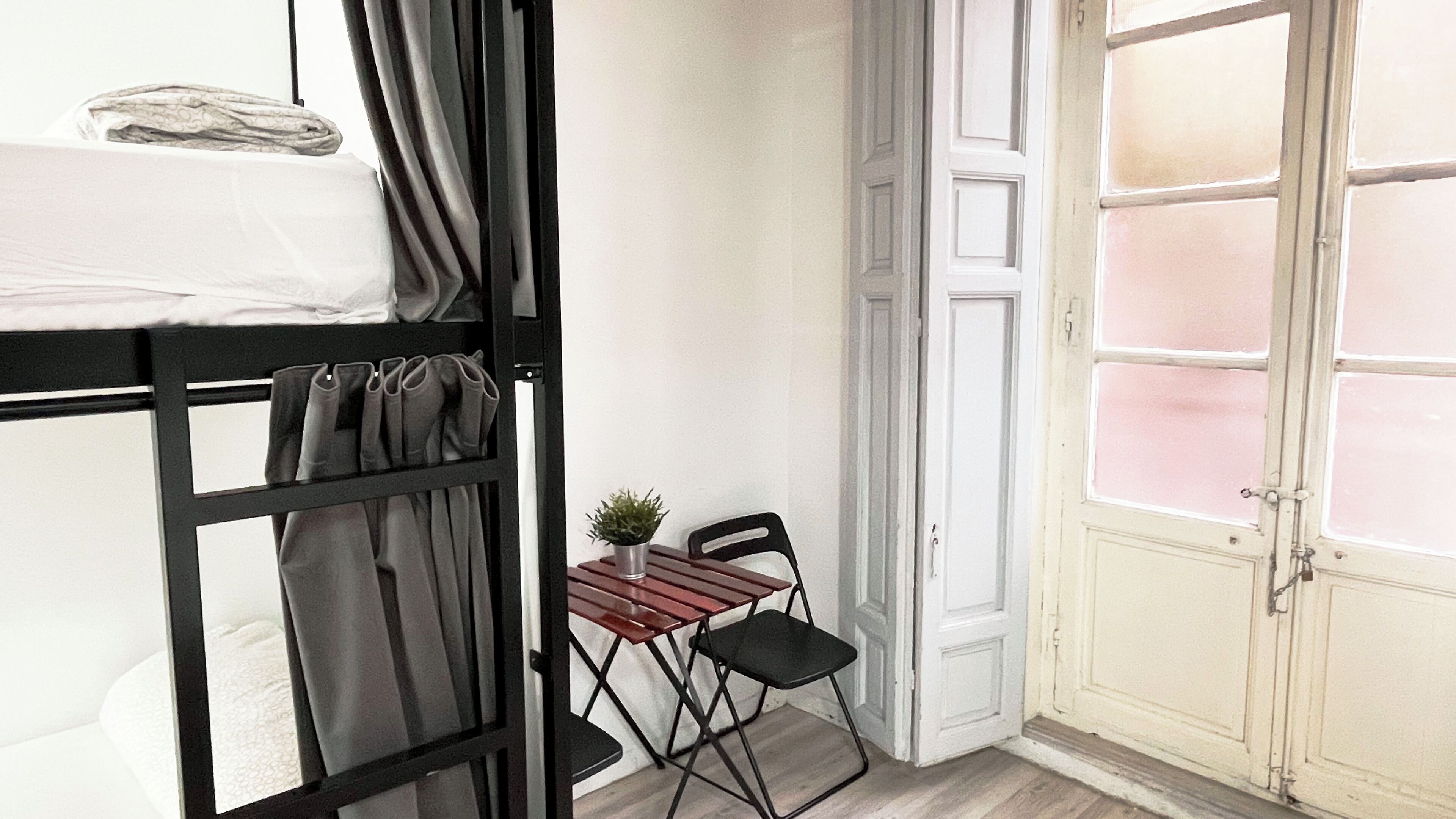 A room with a bunk bed, a small table with a potted plant, two chairs, and a door with frosted glass panels.