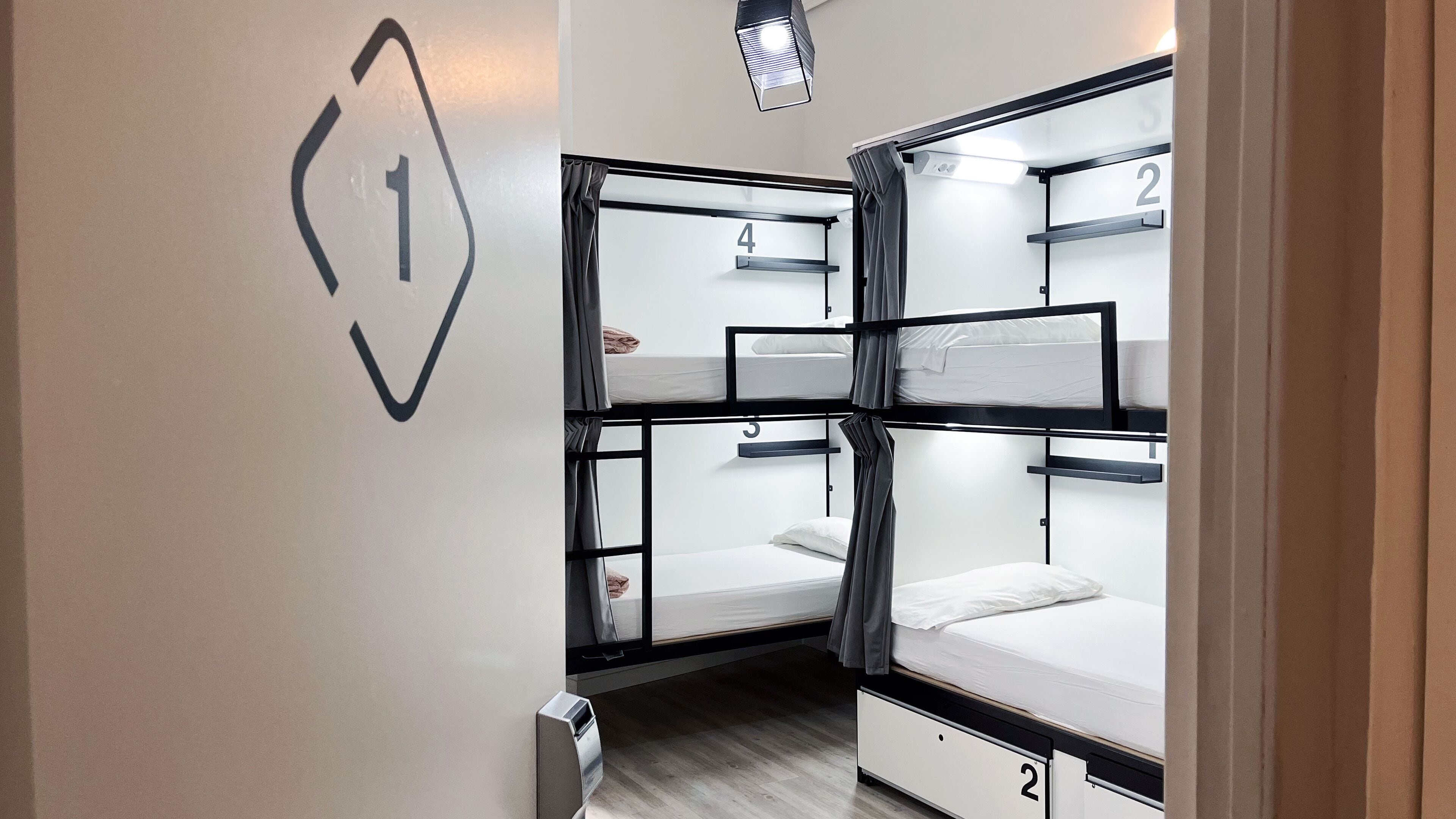 A dormitory room with bunk beds, numbered beds, and a wall-mounted light fixture.