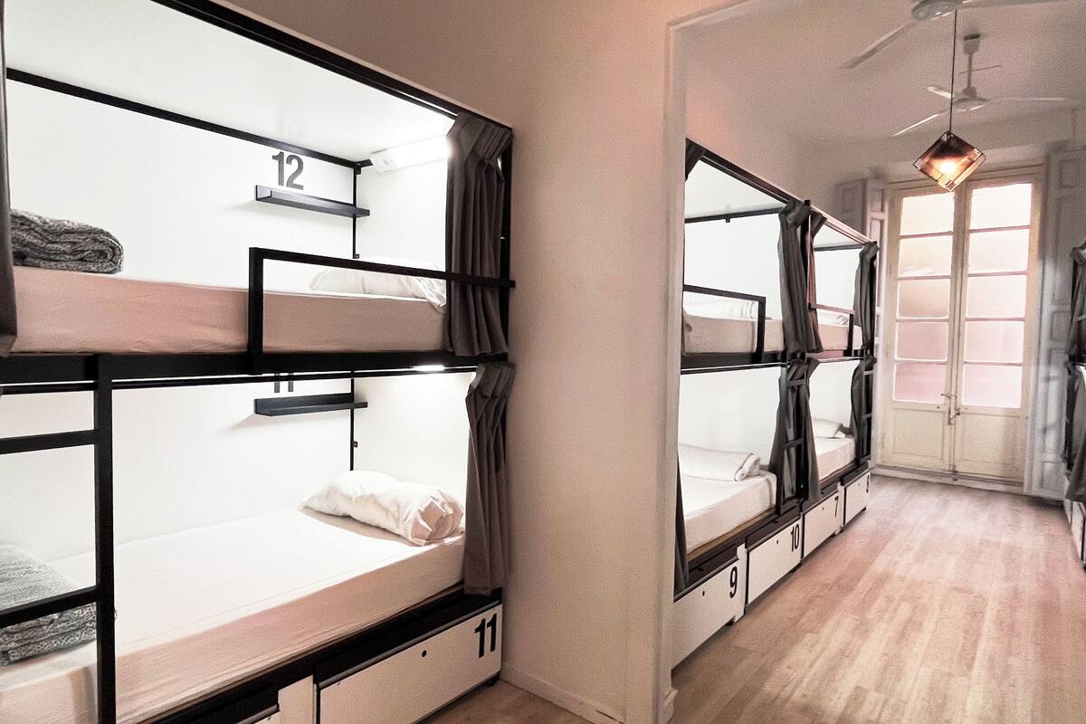 Ein Schlafraum im Mehrbettzimmer-Stil mit Etagenbetten, nummeriert von 9 bis 12, Holzböden und einem Vorhangfenster.